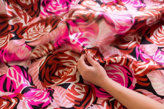 foto di mano che tocca un tessuto rosso con motivi floreali