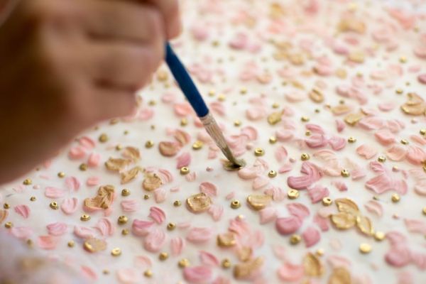 foto dettaglio di una mano che dipinge petali di fiori su tessuto